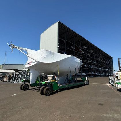 Yacht wrapped in white shrink wrap being moved across a boatyard under a clear blue sky