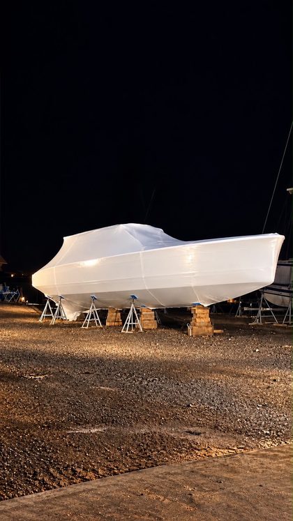 Motor yacht ashore on stands under a fitted white shrink wrap cover, lit at night